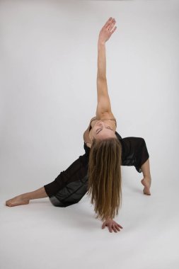 Bir kız dansçı, dans figürlerini bej mayo ve siyah geniş pantolonla modern dans tarzıyla gösterir. Işık arkaplanına yakın plan.