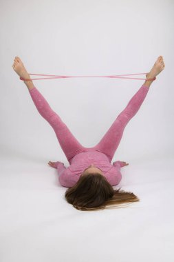 Pembe eşofmanlı bir kız sporcu esneme bandıyla ısınma egzersizleri yapıyor. Işık arkaplanına yakın plan.