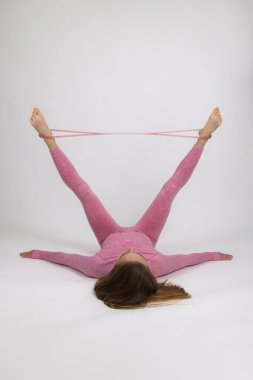 Pembe eşofmanlı bir kız sporcu esneme bandıyla ısınma egzersizleri yapıyor. Işık arkaplanına yakın plan.