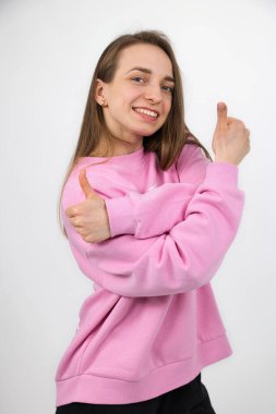 Güzel bir kız iyi bir ruh hali içinde, iki elinin de başparmağıyla bir jest gösteriyor, stüdyo çekimi..