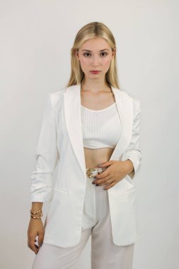 Sarışın, uzun saçlı, model görünümlü, beyaz takım elbiseli, ileriye bakıyor. Beyaz arkaplanda yakın plan.