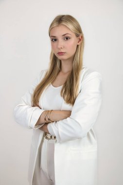 Uzun saçlı, manken görünümlü, beyaz takım elbiseli sarışın bir kız, dikkatle ileriye bakıyor..