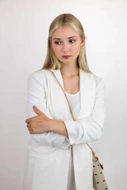 Beyaz takım elbiseli sarışın, üzgün suratlı kameraya poz veriyor. Beyaz arkaplanda yakın plan.