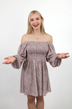 Omzunun dışında bir elbise giymiş neşeli, uzun saçlı sarışın. Kollarını yanlara doğru açmış bir jest yapıyor. Işık arkaplanına yakın plan.