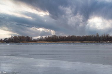 Donmuş bir nehrin kış manzarası bulutlu bir hava ve yerden sarkan büyük gri bulutlar..