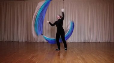 Bir pandomim sahnesi, bir aktris poi yapıyor, uzun bir bez parçası, sahnede, dairesel hareketler yapıyor. Sahne çok renkli yanardöner ışıklarla aydınlatılır..