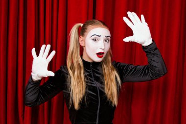 Sahnede yüzünde şaşırmış bir ifadeyle bir pandomim sanatçısı var. Kırmızı bir perdeye yakın plan portre.