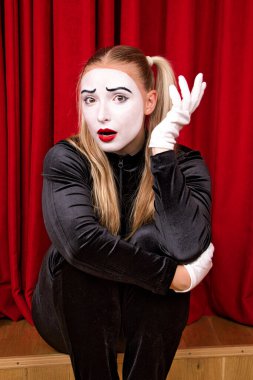 Sahnede, yüzünde sürpriz bir ifade olan bir pandomimci. Kırmızı bir perdeye yakın plan portre.