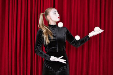 Pandomimci bir sanatçı tiyatro sahnesinde beyaz toplarla çalışır. Kırmızı perdeye yakın çekim..