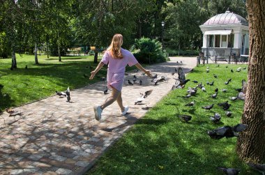 Küçük bir kız parkta güvercinlerin arka planına doğru koşuyor. Güneşli yaz günü.