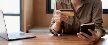 Genç Asyalı bir kadın internet üzerinden alışveriş yapıyor, cep telefonu ve kredi kartı kullanıyor, evden alışveriş yapıyor..