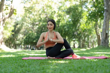 Genç ve çekici bir kız, parkın ortasında spor minderinin üstünde yoga yapıyor.