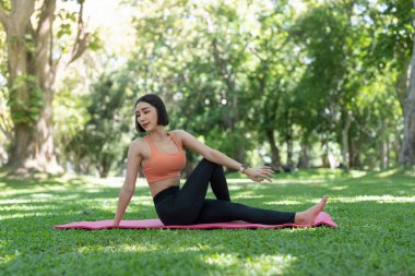 Genç ve çekici bir kız, parkın ortasında spor minderinin üstünde yoga yapıyor.