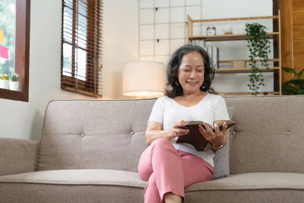 Sonriente Mujer Jubilada Atractiva Leyendo Libro Mientras Está Sentado Sofá —  Fotos de Stock