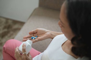 Yaşlı hasta kadın elinde haplarla ilaç şişesinden kapsüller dolduruyor ağrı kesici alıyor, yaşlı insanlar ilaç tedavisi görüyor, görüş açısını kapatıyorlar..