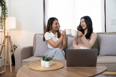 Mutlu Asyalı genç bayan LGBT lezbiyen mutlu çift evdeki oturma odasında dizüstü bilgisayar kullanarak kanepede oturuyor. LGBT lezbiyen çifti birlikte.