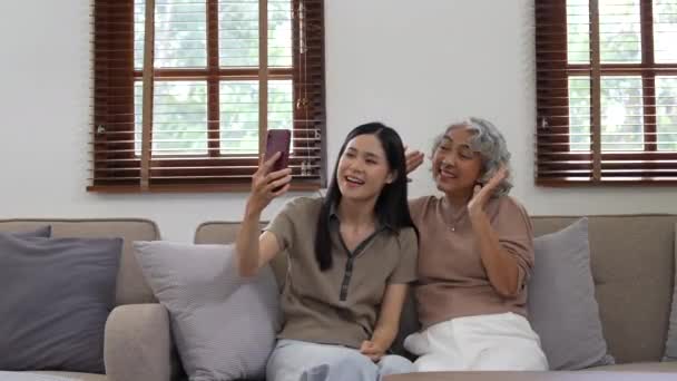 年轻女子和年迈的父母牵着手机打视频电话 看着网上有趣的内容在家里沙发上一起放松 多代同堂的家庭享受现代无线科技的乐趣 — 图库视频影像