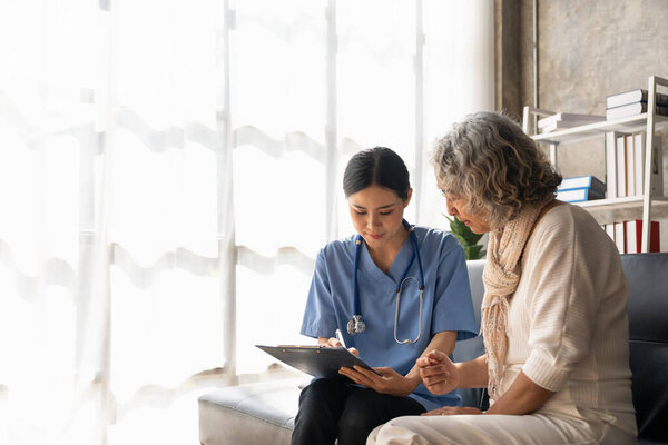 Happy patient is holding caregiver for a hand while spending time together. Elderly woman in nursing home and nurse