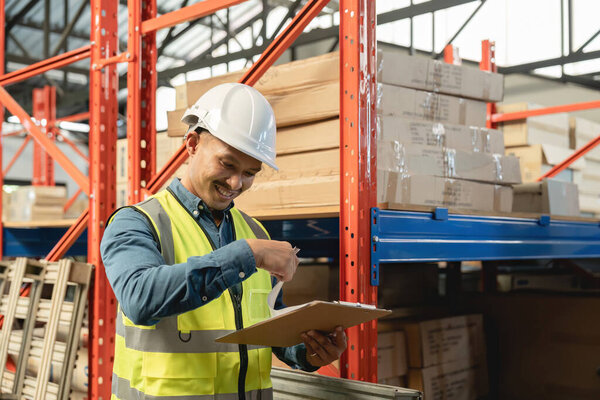 Asian man wearing reflective jacket holding checklist paper standing in factory warehouse