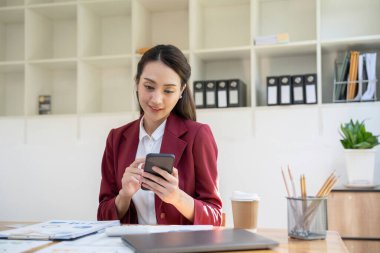 İş yerinde otururken akıllı telefon kullanan gülümseyen Asyalı kadının portresi