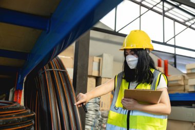 Yansıtıcı ceket giyen Asyalı kadın fabrika deposunda duran kontrol listesi kağıtlarını tutuyor.