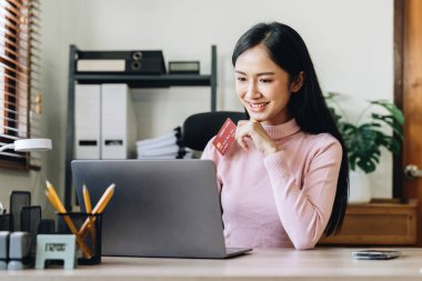 Kredi kartı tutan ve müşteri hizmetlerini telefonla arayan, gülümseyen Asyalı bir kız evde akıllı telefon konuşmalarıyla ödeme yapıyor.