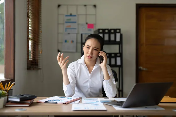 Angry, phone and stressed asian woman on a business call about tax, audit and compliance email on laptop at office desk. Employee working mad, internet and tech glitch on the website of the company