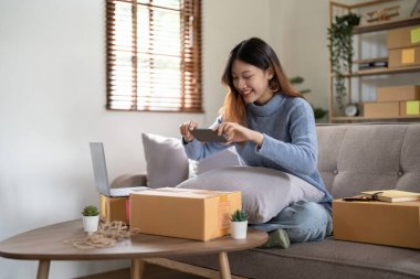 Genç Asyalı bir kadın, internet üzerinden satmak ve paket ürün kutuları hazırlamak için akıllı telefonlardan posta adreslerine fotoğraf çekiyor. KME çevrimiçi fikir konsepti satılıyor.