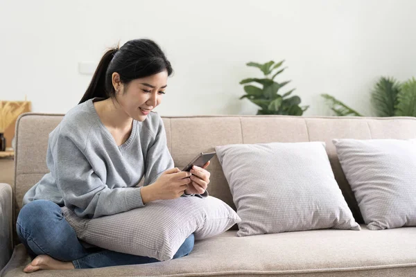 Kanepede Otururken Cep Telefonu Kullanan Gülümseyen Asyalı Bir Kadın — Stok fotoğraf