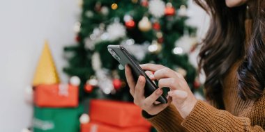 Evdeki cep telefonunu kullanan kadının elini kapat. Boke Noel ağacı arkaplanı.