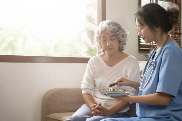 Healthcare worker or caregiver visiting senior woman indoors at home, explaining medicine dosage.