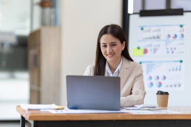 Charming business asian woman working on paperwork financial report while using laptop computer.