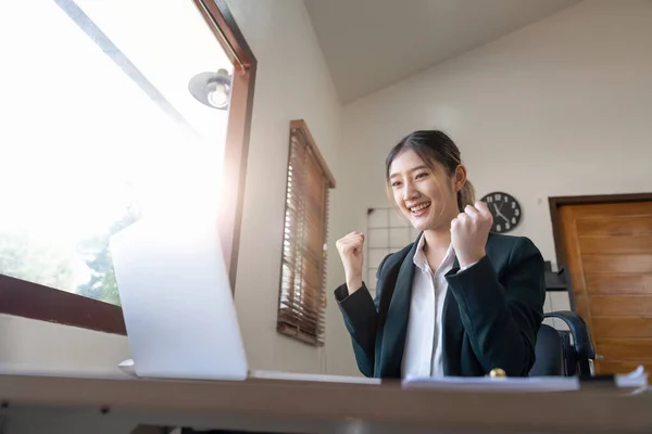 Happy excited successful businesswoman triumphing in office. asian female working on laptop computer.