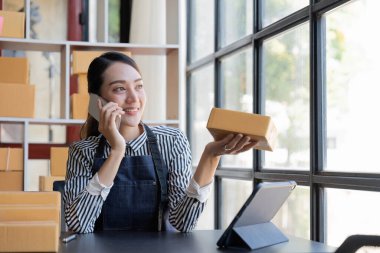Asyalı bir kadın siparişi doğrulamak için bir müşteriyle telefonda konuşuyor, bir online mağazası var, özel bir nakliye şirketi aracılığıyla paketleyip gönderiyor..