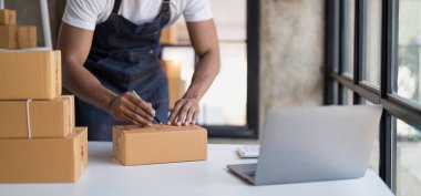 Çevrimiçi alışveriş gençleri iş yerindeki bir karton kutuda küçük bir işe başlıyorlar. Satıcı, müşteri, çevrimiçi satış veya ekommerce için dağıtım kutusunu hazırlar.