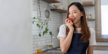 Portrait of Asian young woman look at camera. Attractive beautiful woman wear apron in cozy kitchen with fresh organic vegetables on table cooking healthy vegetable salad, healthy food active life.