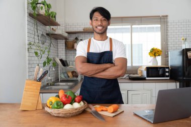 Man in kitchen looking at recipes on laptop while cooking.