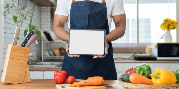 Man in kitchen looking at recipes on tablet.