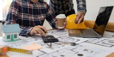 Close up Architect or Engineer using on calculator for calculating value estimating for safety with the drawing construction building.