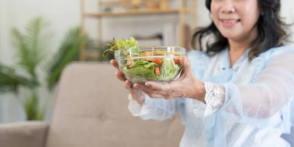 Happy old woman eating healthy vegetable salad at home
