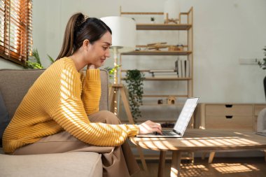 Happy Asian woman while using her laptop in the living room. work from home.