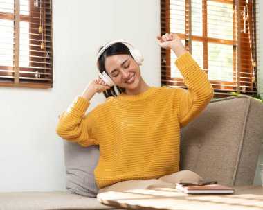 Beautiful Asian woman wearing headphones, enjoying with the music at home.
