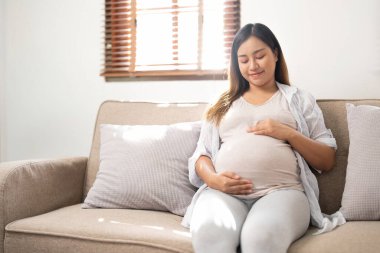 pregnancy, rest, people and expectation concept - close up of happy smiling pregnant woman in and touching her belly at home.