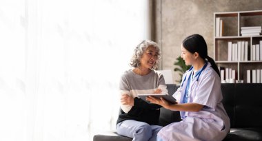Nurse talking with a nursing home patient about his health. The nurse is making notes on a digital tablet.