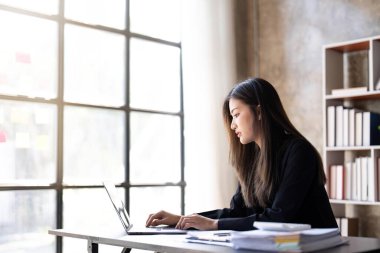 Concentrated young beautiful businesswoman working on laptop and There are documents on the table at bright modern office.