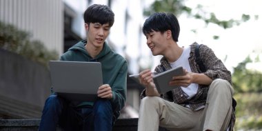Two young Asian male college students discussing and working on their school project together.