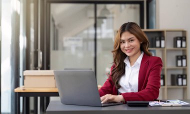 Asian Business woman using laptop and calculator for doing math finance on an office desk, tax, report, accounting, statistics, and analytical research concept.
