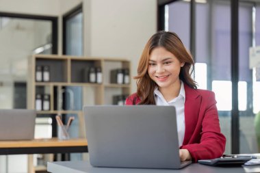 Asian Business woman using laptop and calculator for doing math finance on an office desk, tax, report, accounting, statistics, and analytical research concept.