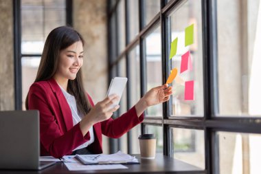 businesswoman talking on cellphone, writing notes on colorful papers in office, employee checking financial documents, working with statistics, consulting client by phone call.