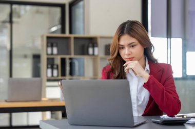 Asian Business woman using laptop and calculator for doing math finance on an office desk, tax, report, accounting, statistics, and analytical research concept.